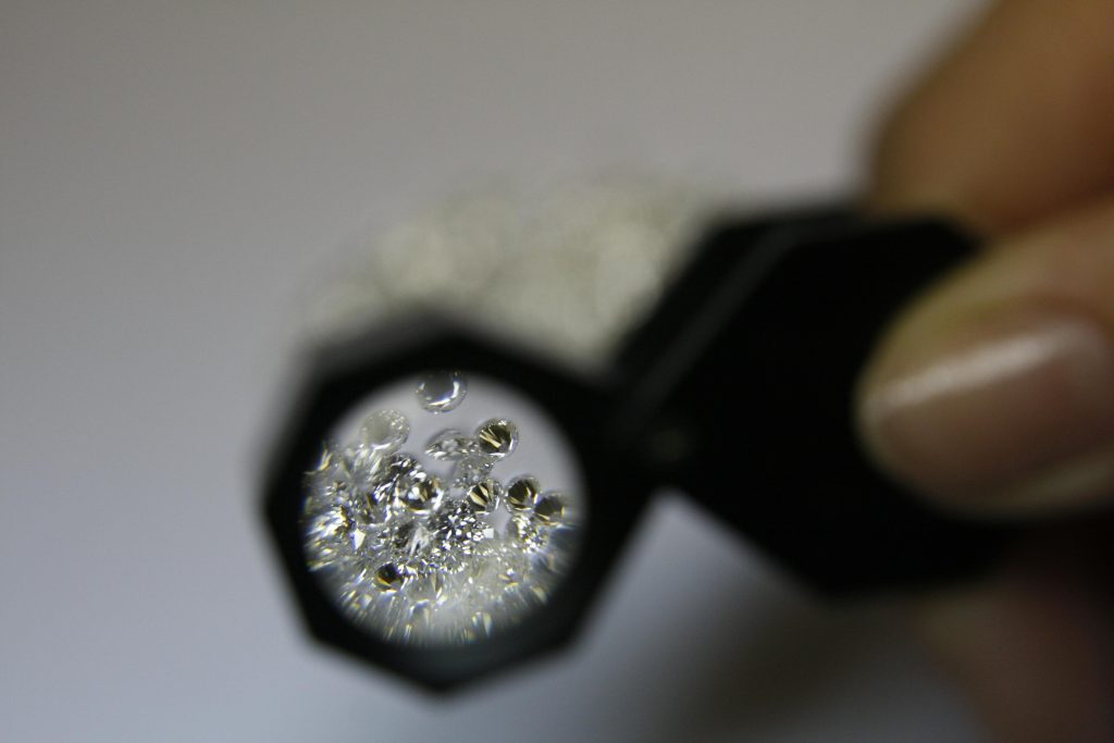 From above closeup of crop anonymous female jeweler with magnifying glass and diamonds in workshop